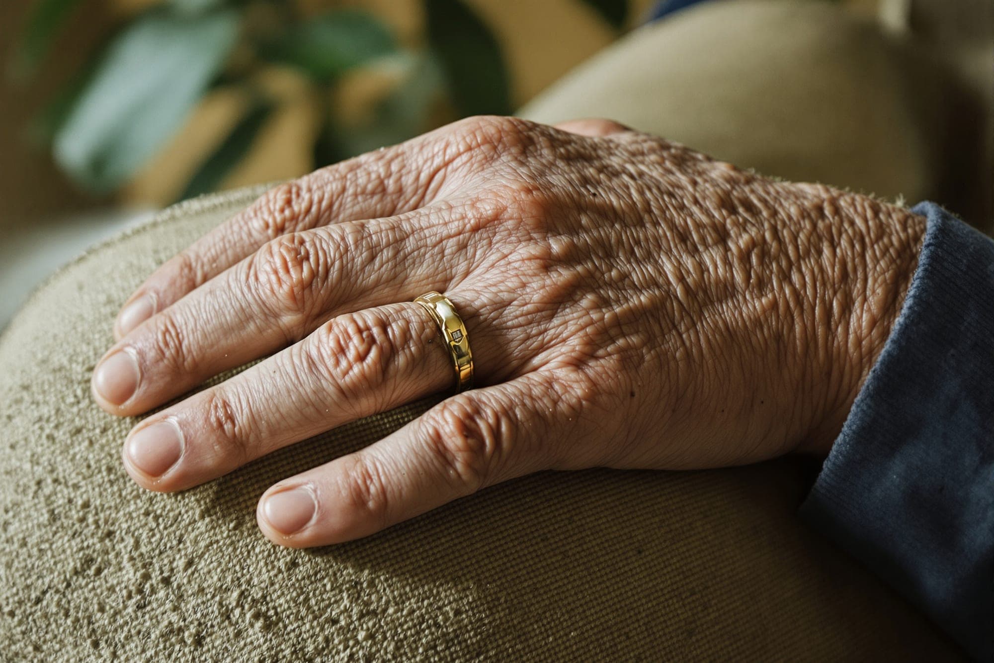 An older person's hand resting gently on a chair in soft window light during a home visit